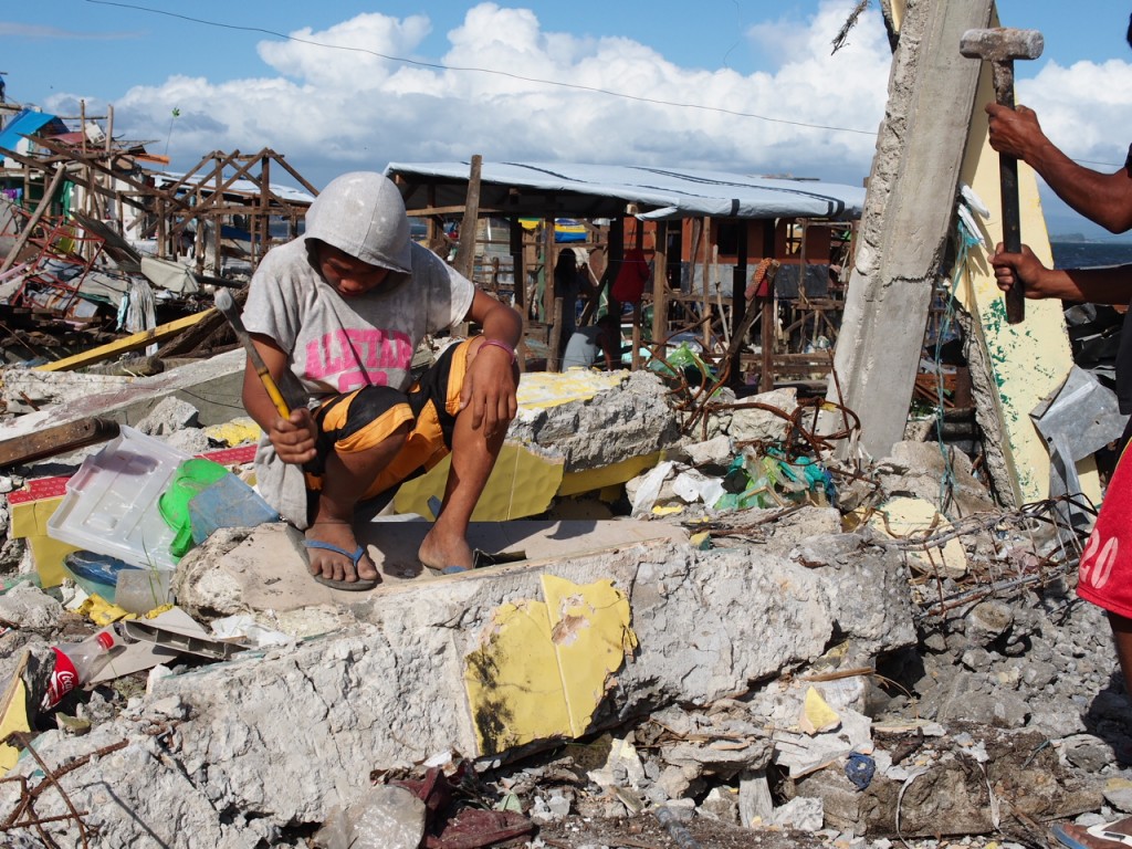 A man chips away at concrete rubble with a framing hammer